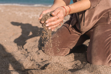 Woman enjoying the warmth of sand by the beach while filtering grains through her hands