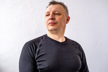 Portrait of a cheerful middle-aged man wearing a gray hoodie, standing against a textured stone wall in natural light.