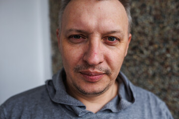 Portrait of a cheerful middle-aged man wearing a gray hoodie, standing against a textured stone wall in natural light.