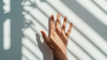 A hand reaching towards sunlight filtering through blinds, casting shadows on a wall.