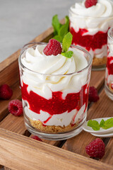 Raspberry trifle with whipped cream, berry sauce, cookie crumbs and mint leaves in a glass on a wooden tray. Summer diet dessert.