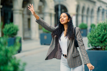 A Confident Young Woman Waving While Standing Outdoors in a Vibrant City Setting