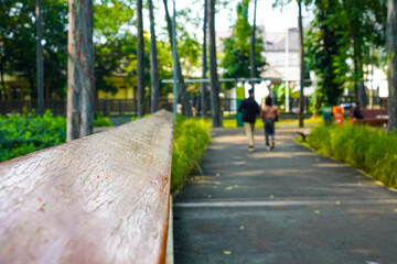 Obraz premium Peaceful Park Walk Featuring Wooden Bench Rail and Green Trees