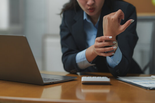 Businesswoman experiencing wrist pain while working on laptop in office