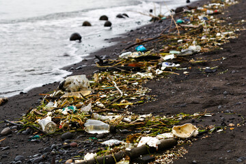 Polluted beach covered with plastic waste, bottles, and debris washed ashore. Environmental damage and ocean pollution concept.
