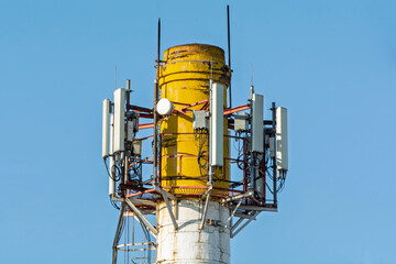 Cellular antennas mounted on an old, cracked industrial chimney with a yellow top, representing...