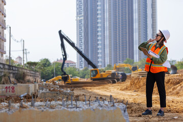 A female construction engineer wearing a safety vest and hard hat inspects a site using a tablet...