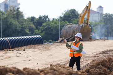 A female engineer wearing a safety vest and hard hat directs work at a construction site. 
