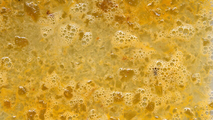 Close-up of solidified fat dispersed in a cooled liquid. The thick, uneven texture with bubbles and small particles forms a rich, gelatinous consistency.