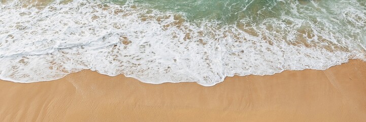 Waves gently wash over golden sand, leaving a foamy white trail. The tranquil movement of water creates a calming and peaceful atmosphere.