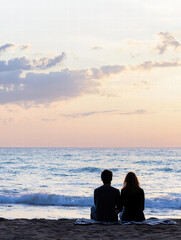 Serene Beachfront: Silhouette of a couple, gazing out at the ocean under a colorful sunset sky, capturing a moment of peace and shared tranquility.