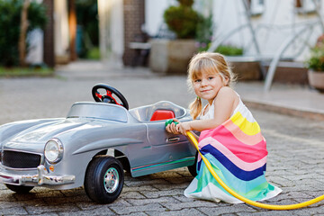 Little toddler girl playing with big vintage toy car and having fun outdoors in summer. Cute child...