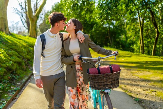 Young couple kissing while walking with bicycle in park