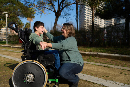 Mother caring for son with disability in wheelchair in park - cerebral palsy concept