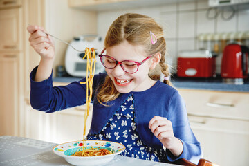 Little school girl eat pasta spaghetti with tomato bolognese with minced meat. Happy preschool...