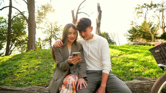 Loving couple sharing smartphone moment, sitting on park bench during golden sunlight, displaying joy and connection while enjoying leisurely afternoon outdoors