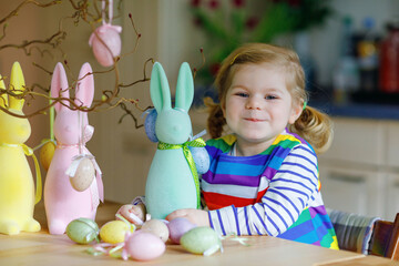 Cute little toddler girl decorating tree and bunny with colored pastel plastic eggs. Happy baby...