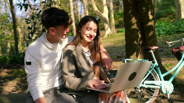 Students enjoying a sunny day in the park, using a laptop and sharing a moment of laughter and complicity