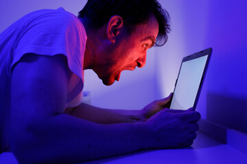 Frustrated Man Yelling at Tablet in Dimly Lit Room at Night