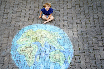 Little preschool girl with earth globe painting with colorful chalks on ground. Positive toddler...