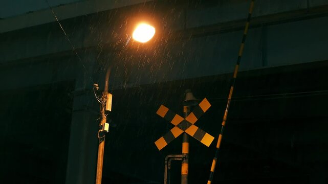 夜に雨が降る踏切が近くにある市街地　外灯