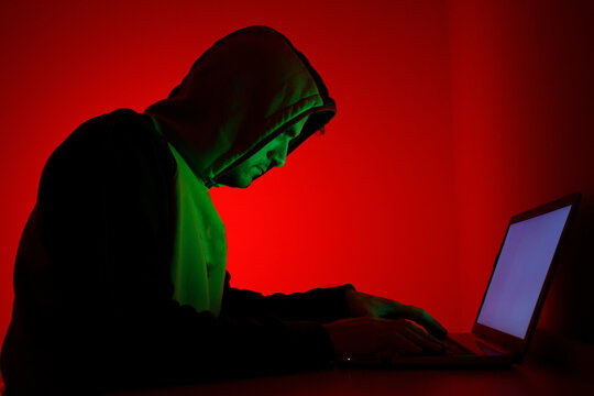 Individual Working Intently on Laptop With Red Background and Green Lighting