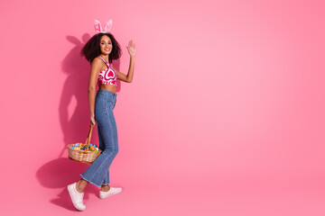Young stylish woman with a basket of colorful eggs and bunny ears against a pink background celebrating seasonal festivities