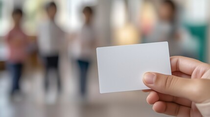 Close-up of fingers holding blank white animator business card mockup with kids playing at birthday party in background