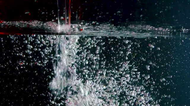 Water is poured into a tank with air bubbles in red light with drops