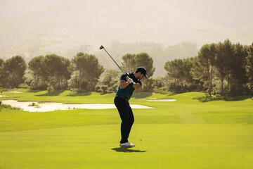 Man playing golf on a sunny day, swinging club and aiming at golf ball near sand bunker on scenic golf course