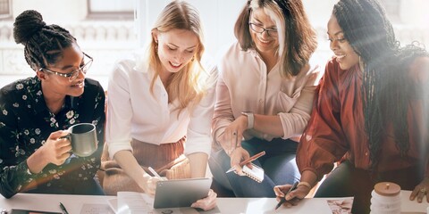 Four diverse business women collaborating in an office. Women working together, sharing ideas. Women in business attire, discussing projects. Professional business women. Diverse working woman.