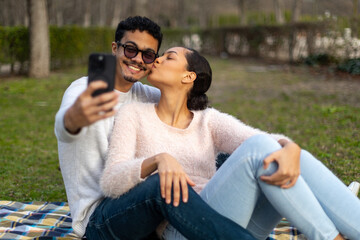 Happy couple taking a selfie in the park while kissing