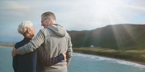 Fototapeta premium Elderly Caucasian couple, man and woman, embracing by the sea. The elderly couple enjoys the scenic view, with the man and woman sharing a loving moment by the sea. Senior couple hugging by the sea
