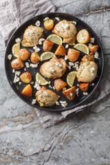 Greek chicken baked with feta, garlic and lemon zest with potatoes close-up in a frying pan on the table. Vertical top view from above