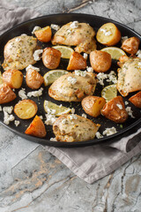Greek chicken baked with feta, garlic and lemon zest with potatoes close-up in a frying pan on the table. Vertical