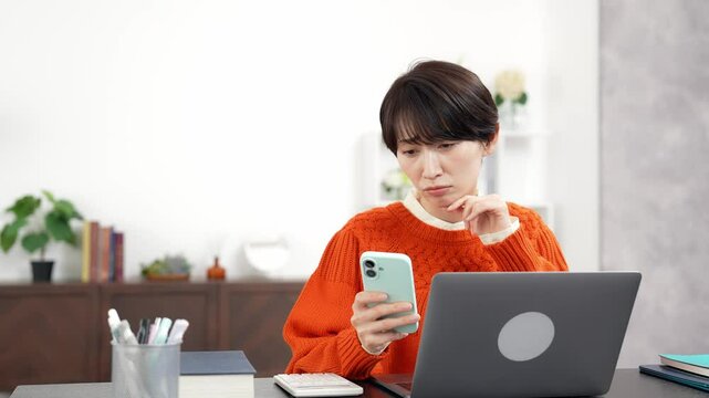 スマホとノートパソコンを見ながら悩むミドル女性
