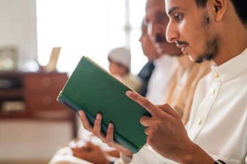 A muslim person reading a green book, focused and engaged. The book is held with both hands, indicating concentration. The setting is calm and peaceful.