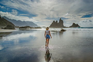 A woman stands still on the wet sand at Playa Benijo, Tenerife, with the ocean breeze in her hair and the sound of waves filling the air © Anna Lurye