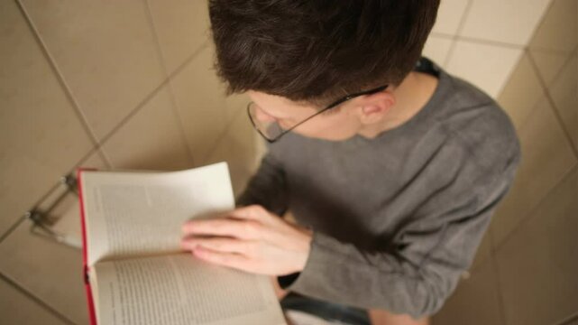 Engrossed reader on the toilet. A man gets so absorbed in an interesting book that he loses track of time, forgetting everything else. A funny everyday situation for a true book lover.