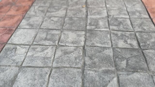 Close-up texture of concrete path showing rough surface with small stones, cracks, and natural imperfections.
