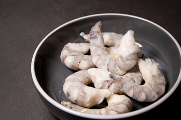 Frozen raw tiger prawns shrimps in a grey bowl on grey kitchen table 