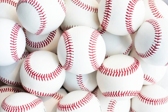 A collection of baseballs with red stitching. Baseballs stacked together background. Close-up of baseballs. White baseballs with red stitching. Sports equipment. Sports background.