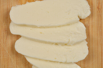 Sliced mozzarella cheese is arranged on a wooden cutting board, ready for use in cooking