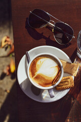Coffee and biscuit outdoor on a sunny autumn day in a cafe, cozy autumn scene with leaves and sunglasses