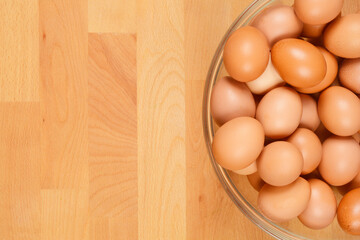 A top-down view of a clear glass bowl filled with brown eggs, set against a light wooden surface
