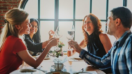Group of people enjoying a meal, toasting with wine glasses. Diverse group, cheerful atmosphere, dining together, celebrating with friends. Group celebration and party.