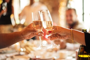 Close-up of hands toasting with champagne glasses at celebration party. Festive celebration with...