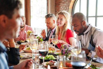 Group dining at a restaurant, diverse people enjoying a meal together, sharing food and conversation, lively atmosphere with wine and laughter. Diverse people having dinner at a restaurant.
