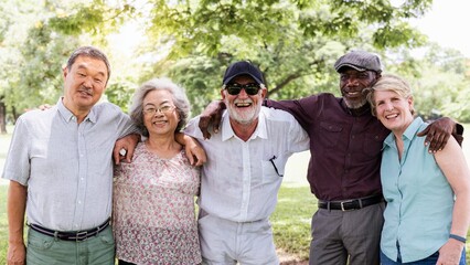 Diverse group of senior friends smiling and enjoy outdoors. Happy seniors enjoying nature in the park. Diverse group of senior men and women hugging each other at park. Happy old people outdoor