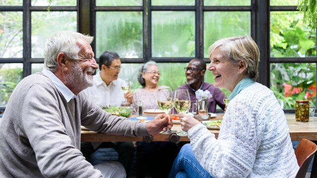 Group of diverse seniors enjoying a meal together, laughing and sharing wine. Elderly friends, diverse gathering, happy seniors, enjoying life, sharing moments. Senior friends in dinner gathering.